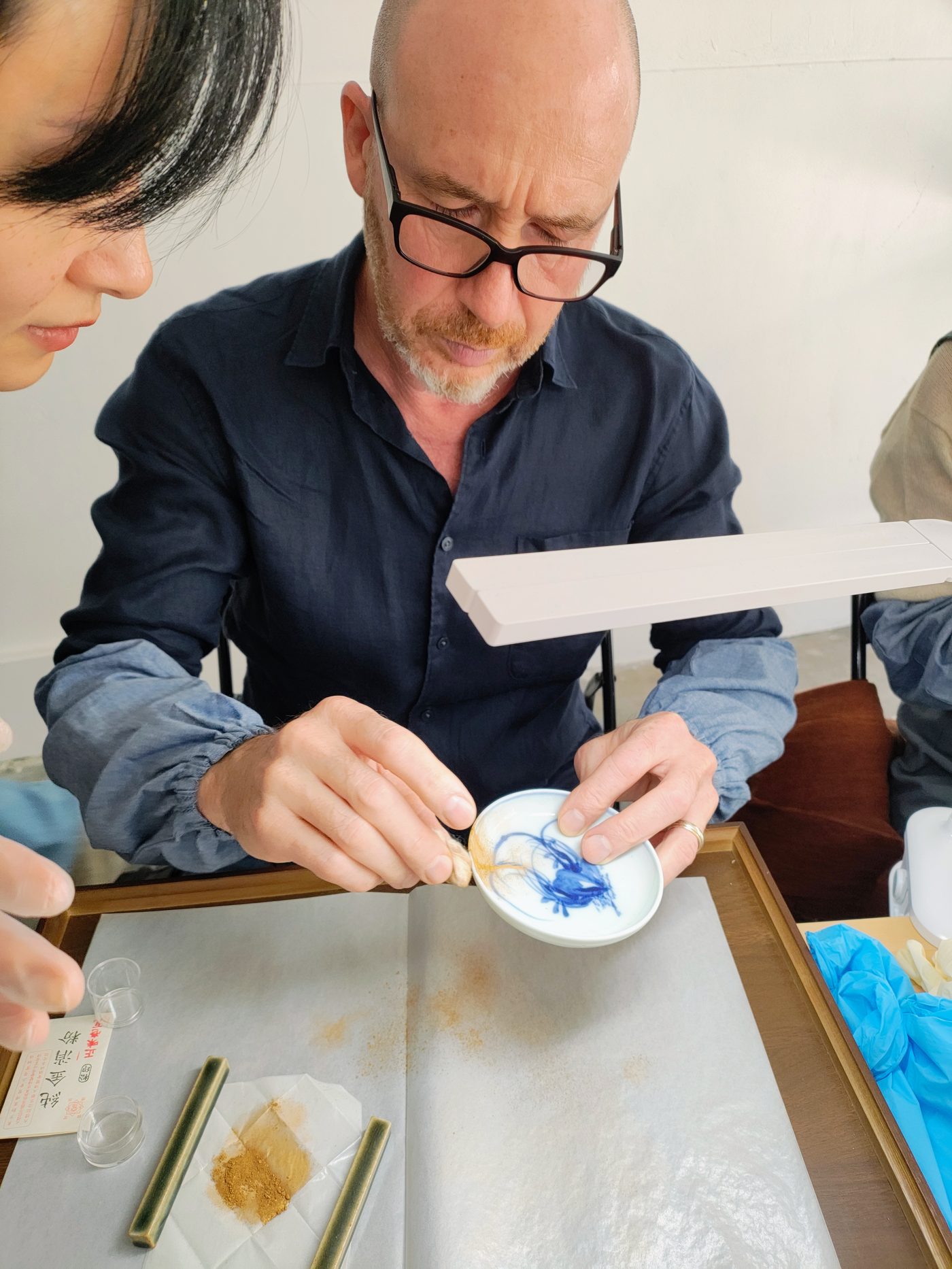 A guest painting urushi along the seam of a small dish under a lamp
